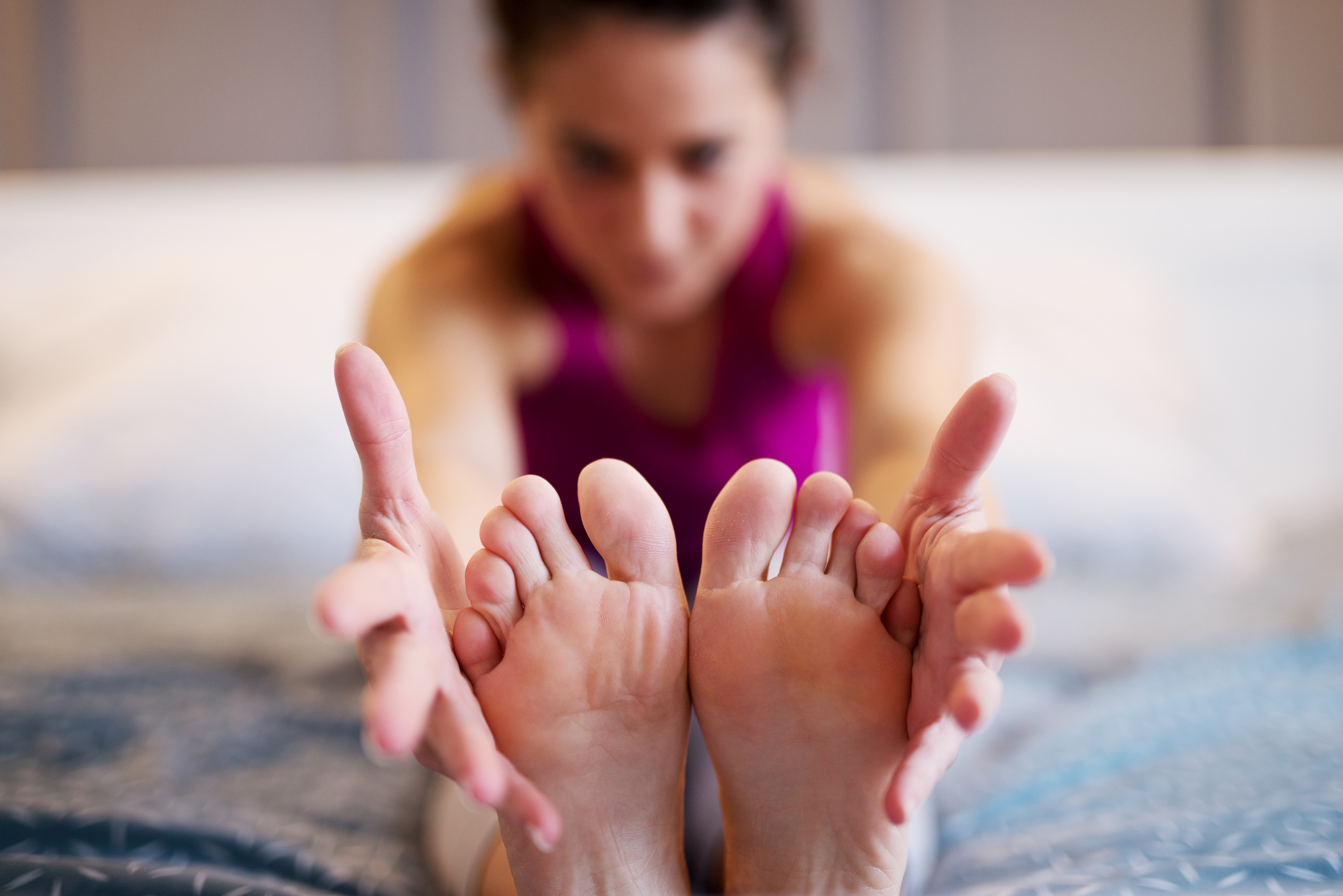 Middle aged woman stretching yoga exercise while sitting forward on the bed while her hands are holding the feets. Focus on the feets and hands.